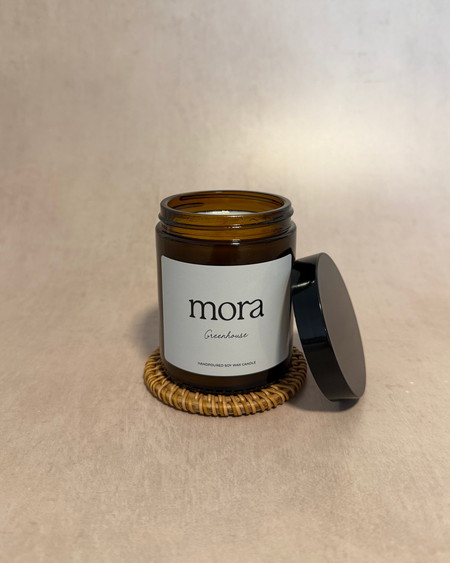 Candle jar with 'mora' label on a beige surface