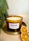 Candle with 'mora' label on a gold tray with dried oranges and greenery