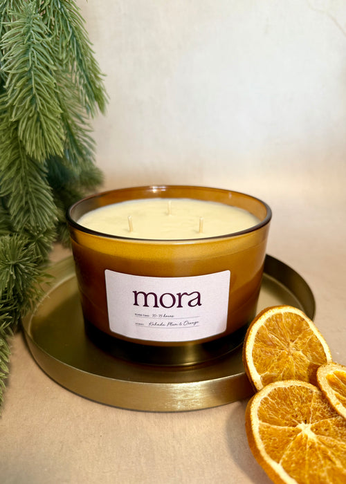 Candle with 'mora' label on a gold tray with dried oranges and greenery
