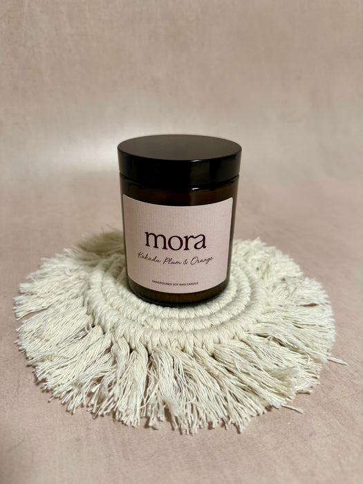 Candle jar labeled 'mora' on a textured surface with a beige background