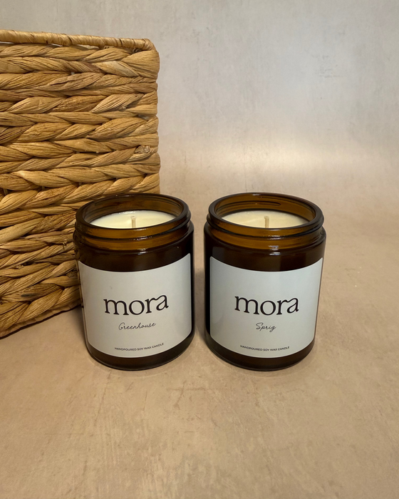 Two 'mora' candles on a beige surface with a woven basket in the background.